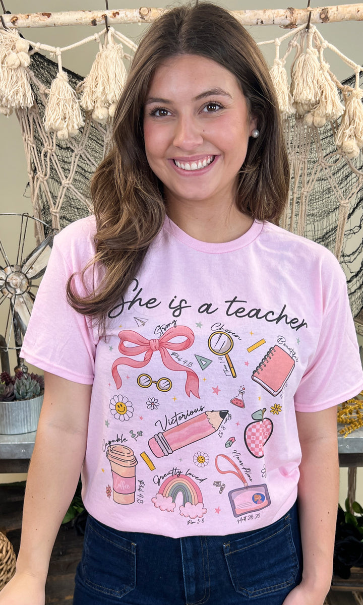 Cheerful woman wearing a She is a Teacher Graphic Shirt, showcasing playful educational designs in pink. Perfect for educators!