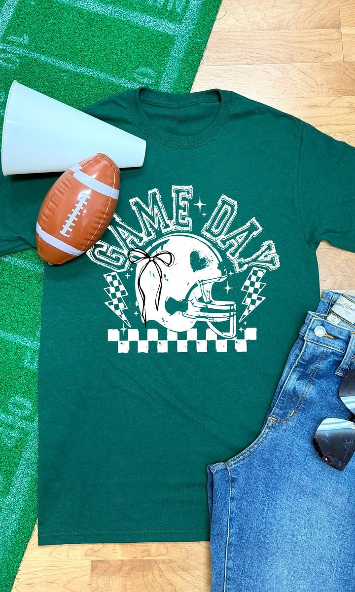 Green Game Day Football Bow Graphic T-Shirt displayed with football, megaphone, and denim shorts for a perfect game day look.