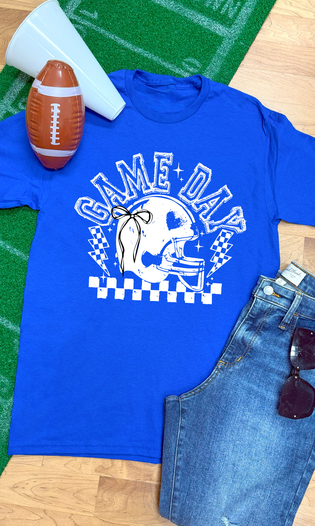 Bright blue Game Day Football Bow Graphic T-Shirt styled with football accessories, perfect for game day fun.