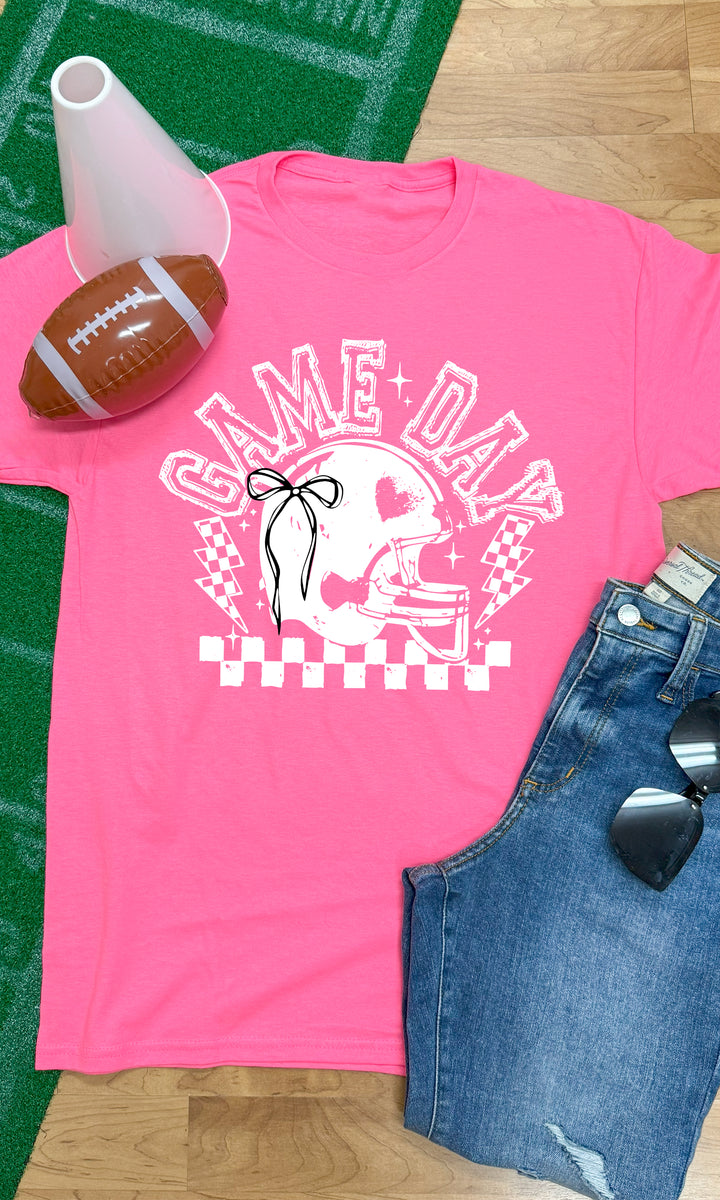 Bright pink Game Day Football Bow Graphic T-Shirt displayed with a football and shorts, perfect for game day outfits.