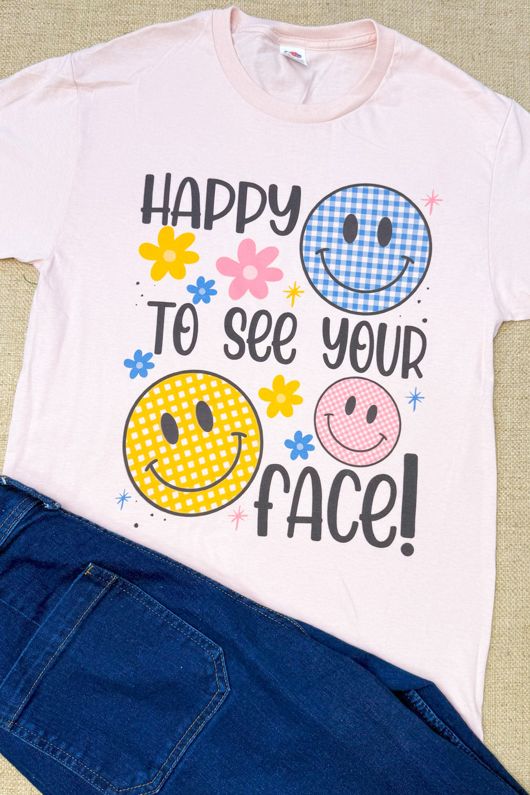 Happy To See Your Face Graphic Shirt featuring colorful smiley faces and flowers, perfect for a cheerful outfit.